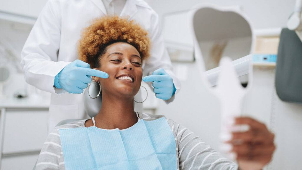 Patient at Cox Family Dentistry smiling after a successful dental crown or filling treatment, with the dentist pointing at her restored tooth during a dental checkup.